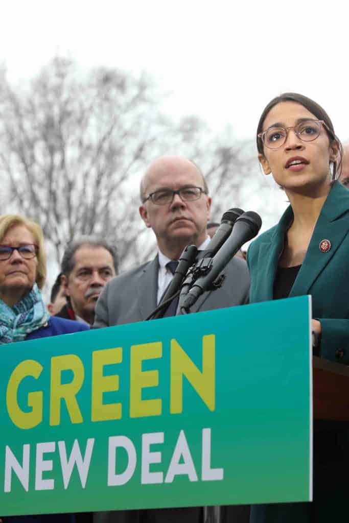 Alexandria Ocasio-Cortez speaks above a sign labeled "The Green New Deal", a political program designed to combat climate change