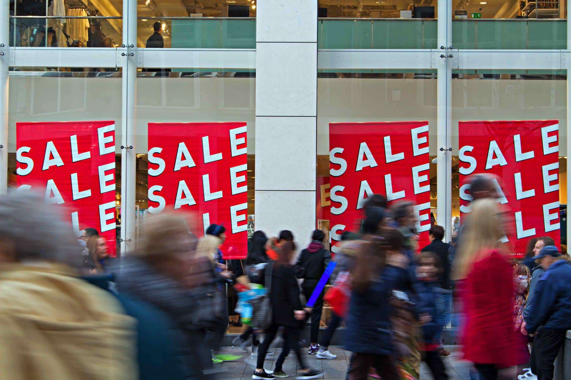 People walk by garish billboards advertising a sale, showing how society is assaulted by consumerism