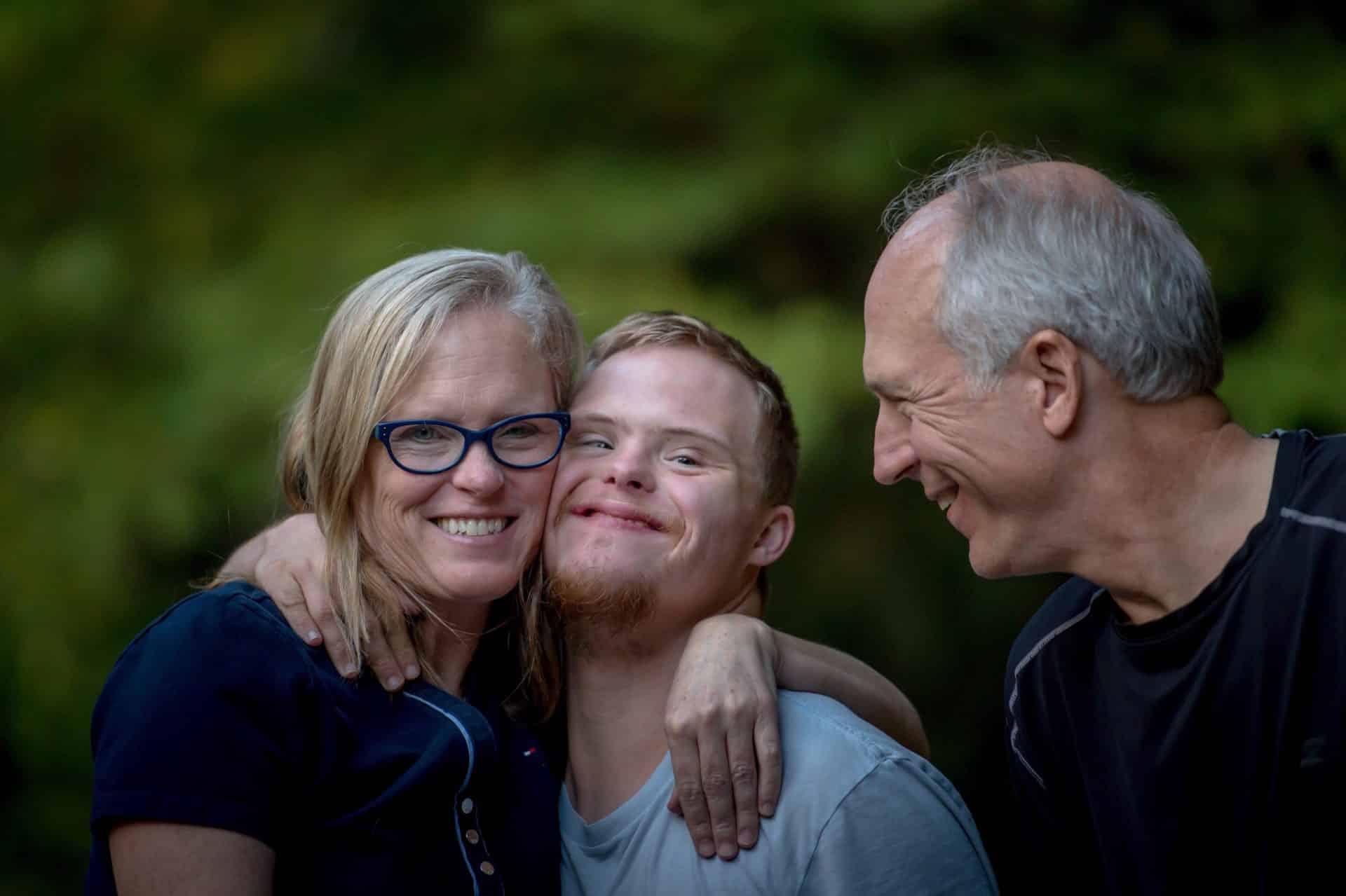 Two parents smile for photos with their son who has down-syndrome