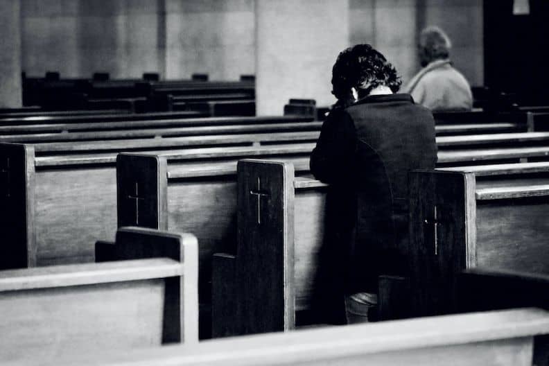A woman prays in the pews of a mostly empty Church, showing how combatting racism in the United States must be a spiritual battle